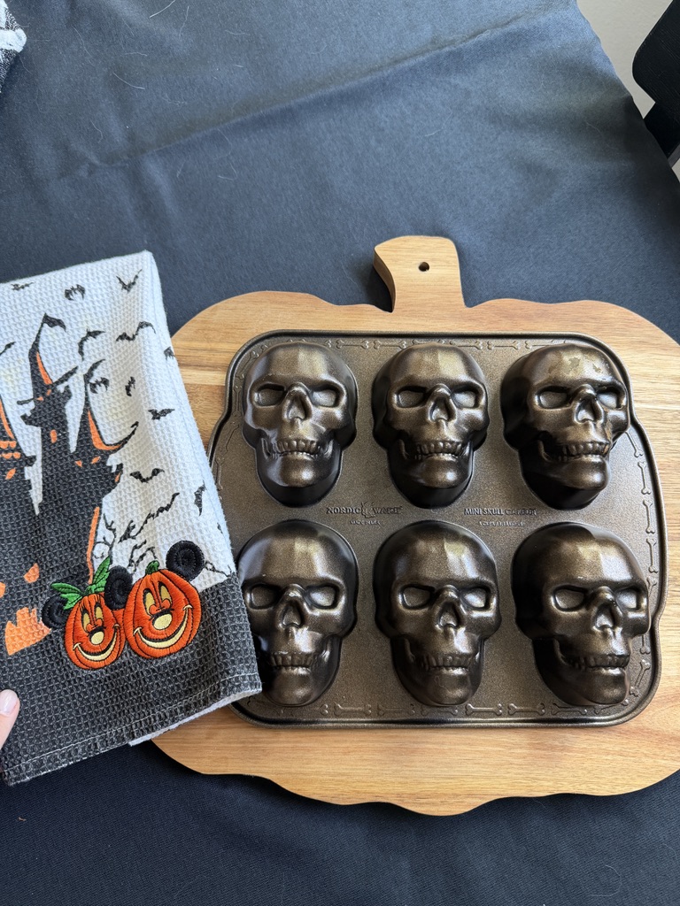 Six-skull Nordic Ware pan on a pumpkin-shaped wooden board beside a Halloween kitchen towel