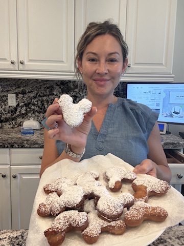 Stephanie smiling in her kitchen, holding a tray of powdered-sugar treats